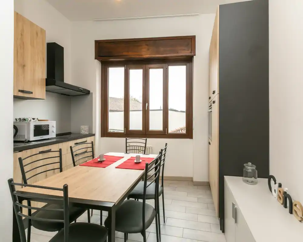 Bright, modern kitchen with a wooden dining table for six, integrated cabinets and a large window providing natural light — ideal for casual meals.