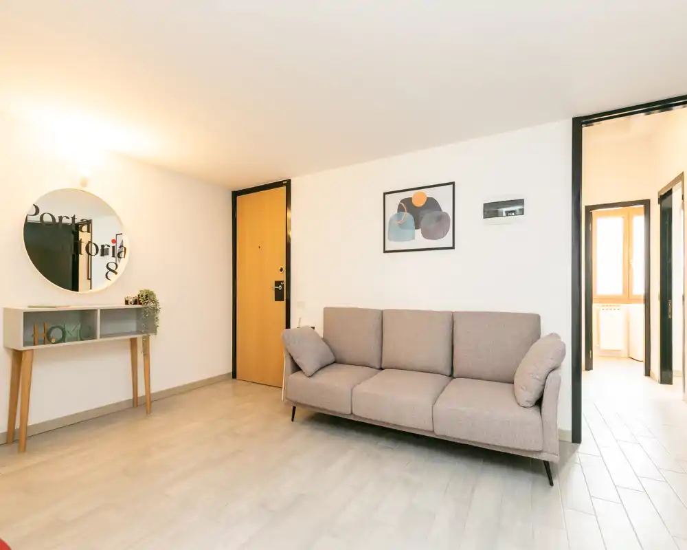 Bright, modern living room with a three-seater sofa, decorative wall art and a small console table with mirror — clean, softly lit space ideal for relaxing.