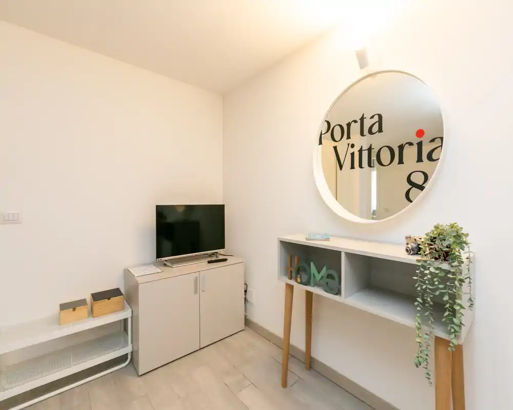 Compact, well-lit living area with a TV cabinet, decorative console table and round mirror; minimal, modern styling ideal for a small rental.