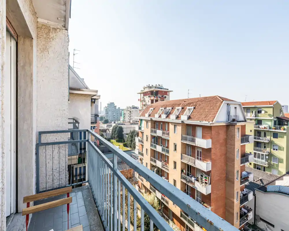Balcón soleado con barandilla metálica que mira a edificios residenciales y al paisaje urbano — ideal para el café de la mañana o una pequeña zona de descanso.