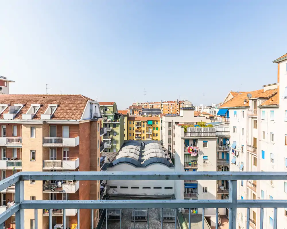 Balcón soleado con vistas a edificios y tejados colindantes, ideal para mostrar una terraza exterior con vistas a la ciudad.