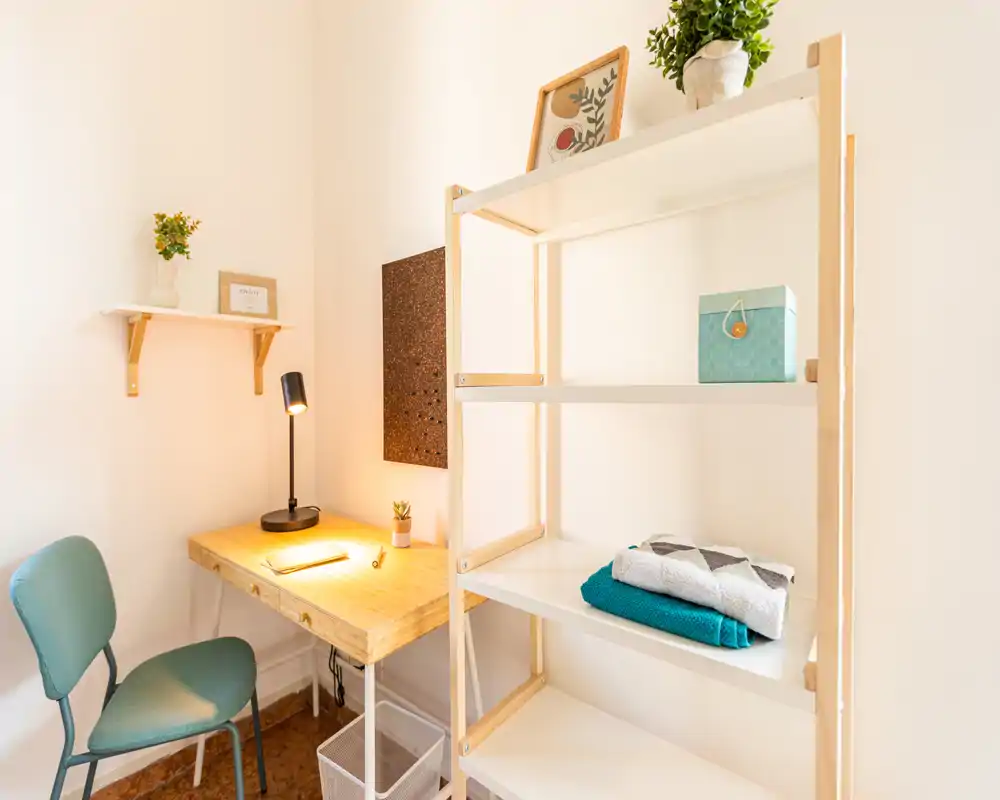 Coin salon/bureau compact et lumineux avec bureau en bois, lampe chaleureuse et étagères ouvertes — idéal pour un studio.