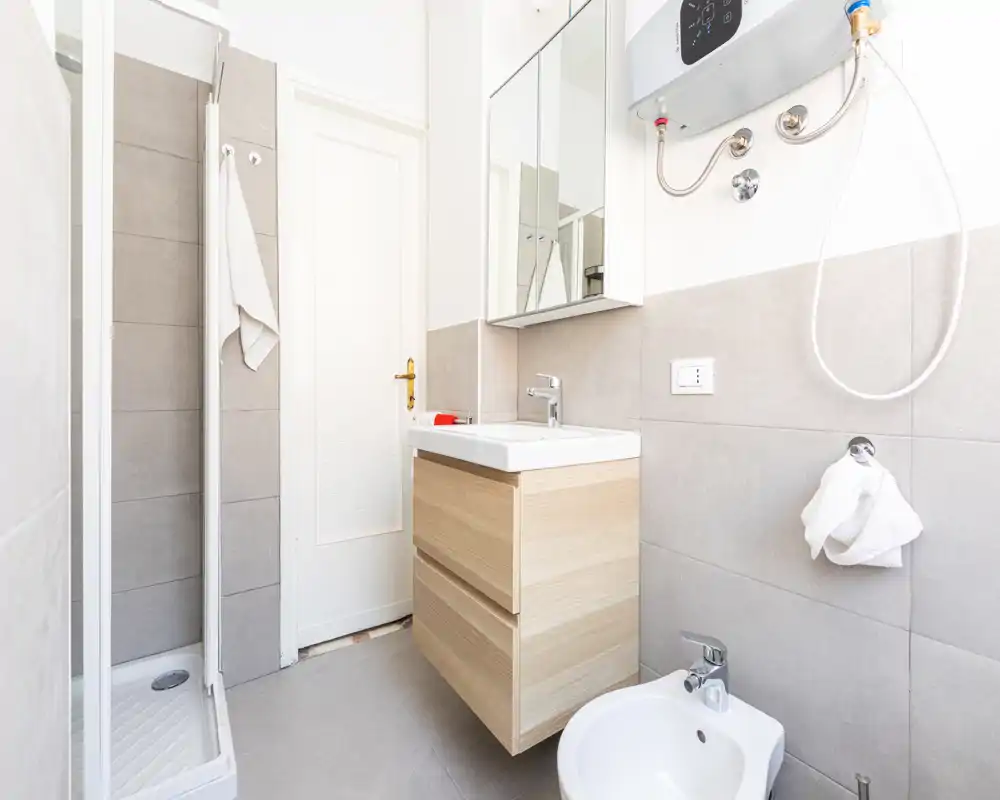 Bright, modern bathroom with a shower stall, wall-mounted sink cabinet, bidet and mirrored medicine cabinet; neutral grey tiles and clean white fixtures create a fresh look.