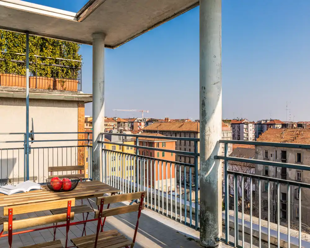 Sunny balcony with a wooden table and folding chairs, enjoying a wide city view — bright, airy outdoor space ideal for morning coffee or relaxing.