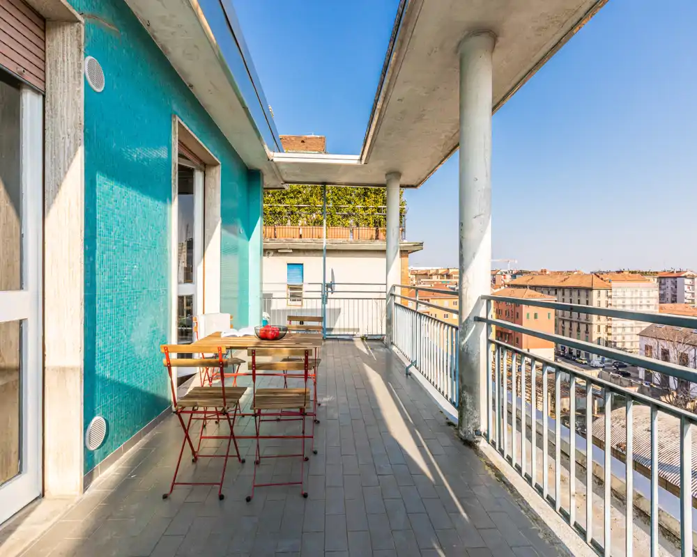 Sunny furnished terrace with a small dining table and folding chairs, overlooking the city; ideal for outdoor meals and relaxation with clear daylight and open views.