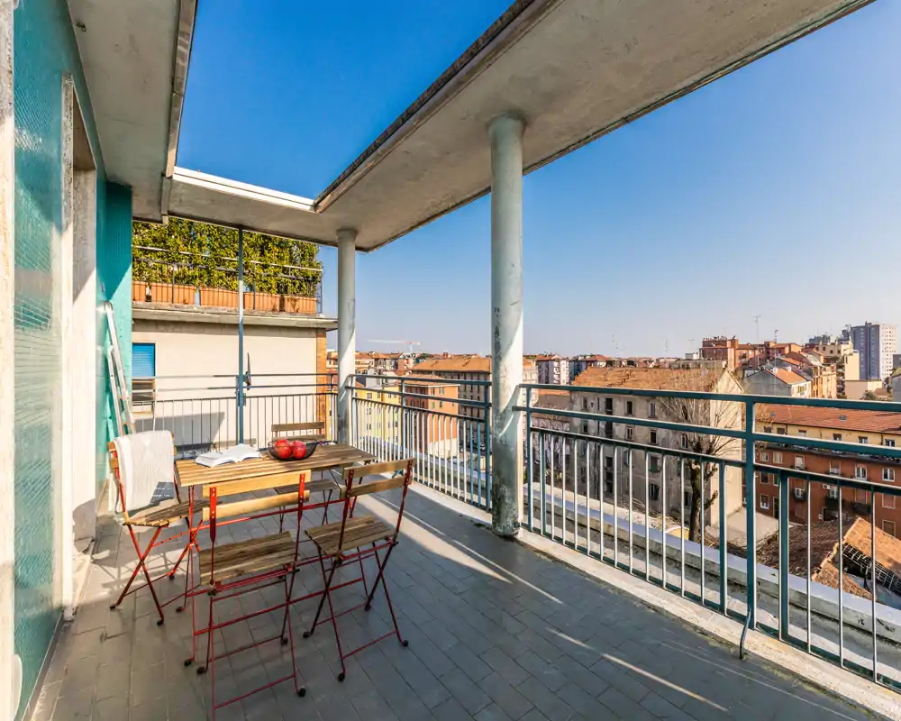 Sunny furnished terrace with a wooden table and folding chairs, overlooking city rooftops — ideal for outdoor dining and relaxing.