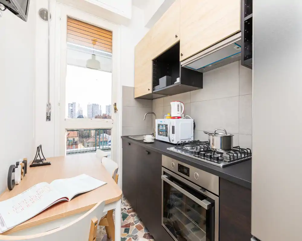 Bright, compact kitchen with modern appliances, a gas hob and oven, microwave and a small dining table by a large window offering city views.