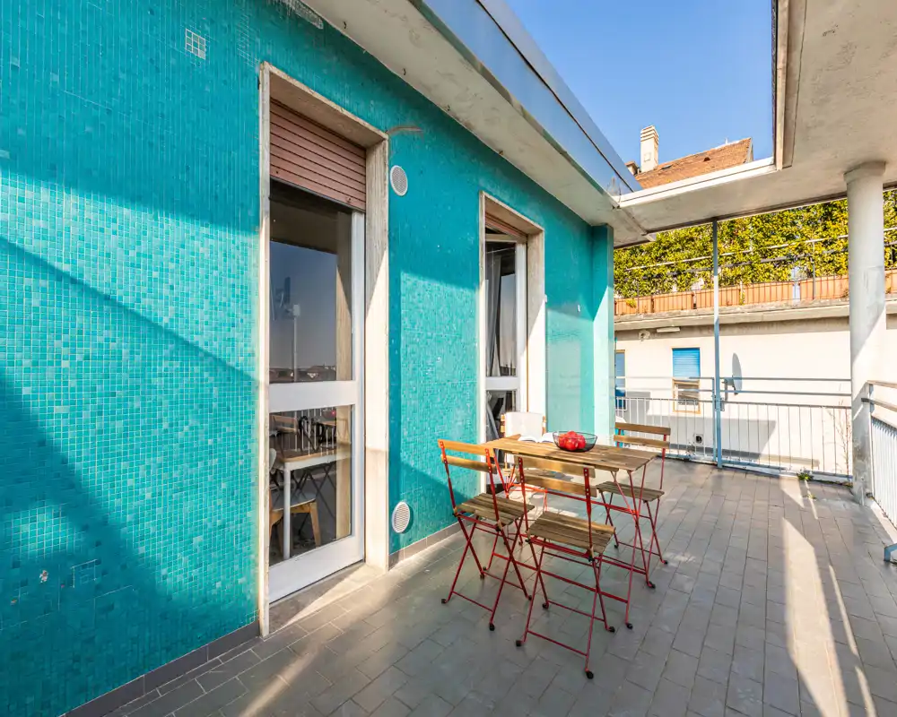 Sunny private terrace with a turquoise tiled wall, folding table and chairs — an ideal spot for outdoor dining and relaxing.