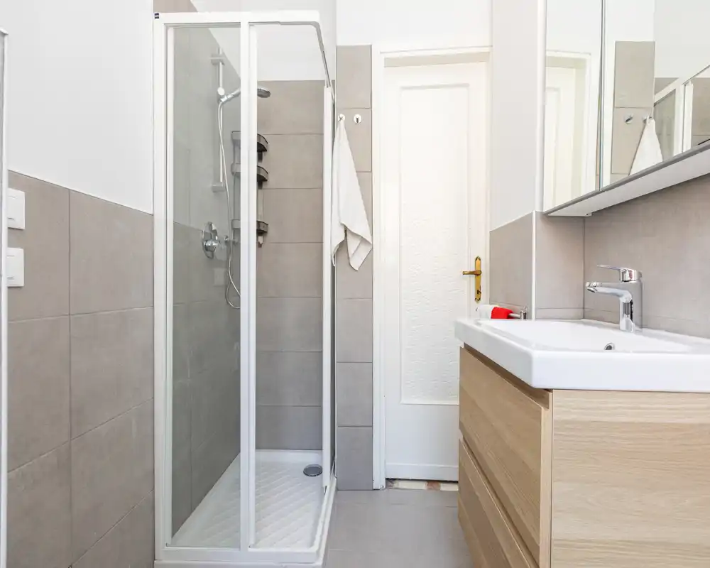Bright, modern bathroom with a glass-enclosed shower, wall-mounted fixtures and a wooden vanity with sink.