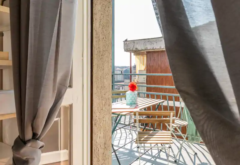 Balcon ensoleillé avec petite table en bois et chaises pliantes, décoré d’un vase et d’une fleur — idéal pour le café du matin.