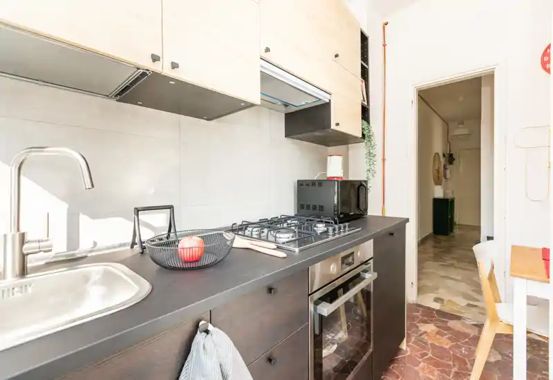 Cuisine moderne et lumineuse avec évier en inox, plaque à gaz et four encastré. Les meubles clairs et le plan de travail foncé offrent un contraste contemporain ; quelques touches décoratives rendent l'espace chaleureux.