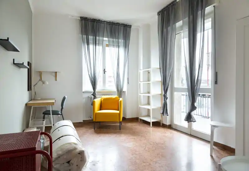 Zona de estar luminosa y minimalista con un butacón amarillo llamativo junto a grandes ventanas y un pequeño escritorio — ideal para relajarse o trabajar con luz natural.