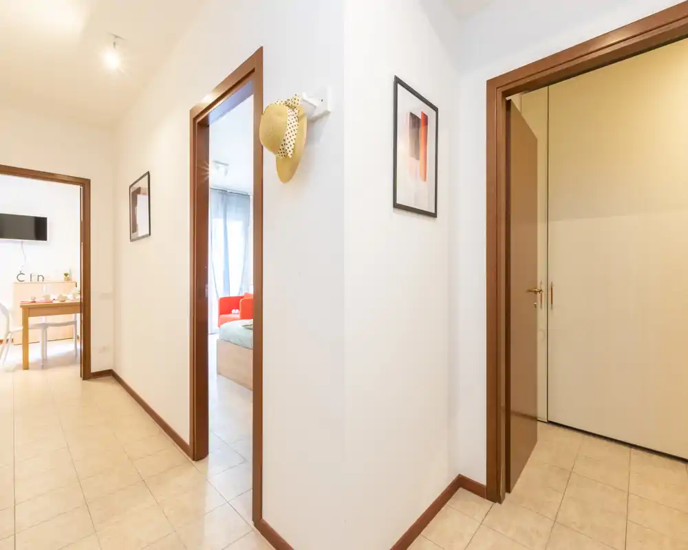 Pasillo/entrada luminoso con suelo de baldosas y varias puertas que comunican con el salón y el dormitorio; paredes neutras y cuadros sencillos que crean un espacio limpio.