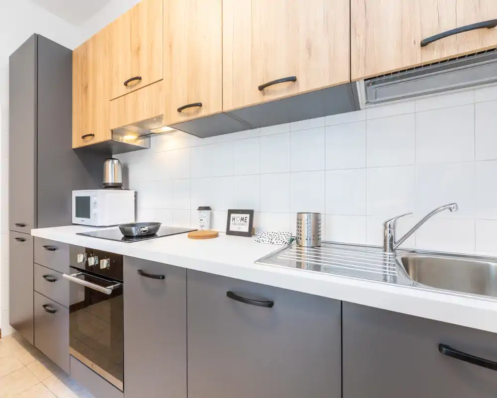 Cocina moderna y luminosa con electrodomésticos integrados, fregadero y encimera ordenada; muebles en madera clara y gris para un aspecto contemporáneo y limpio.
