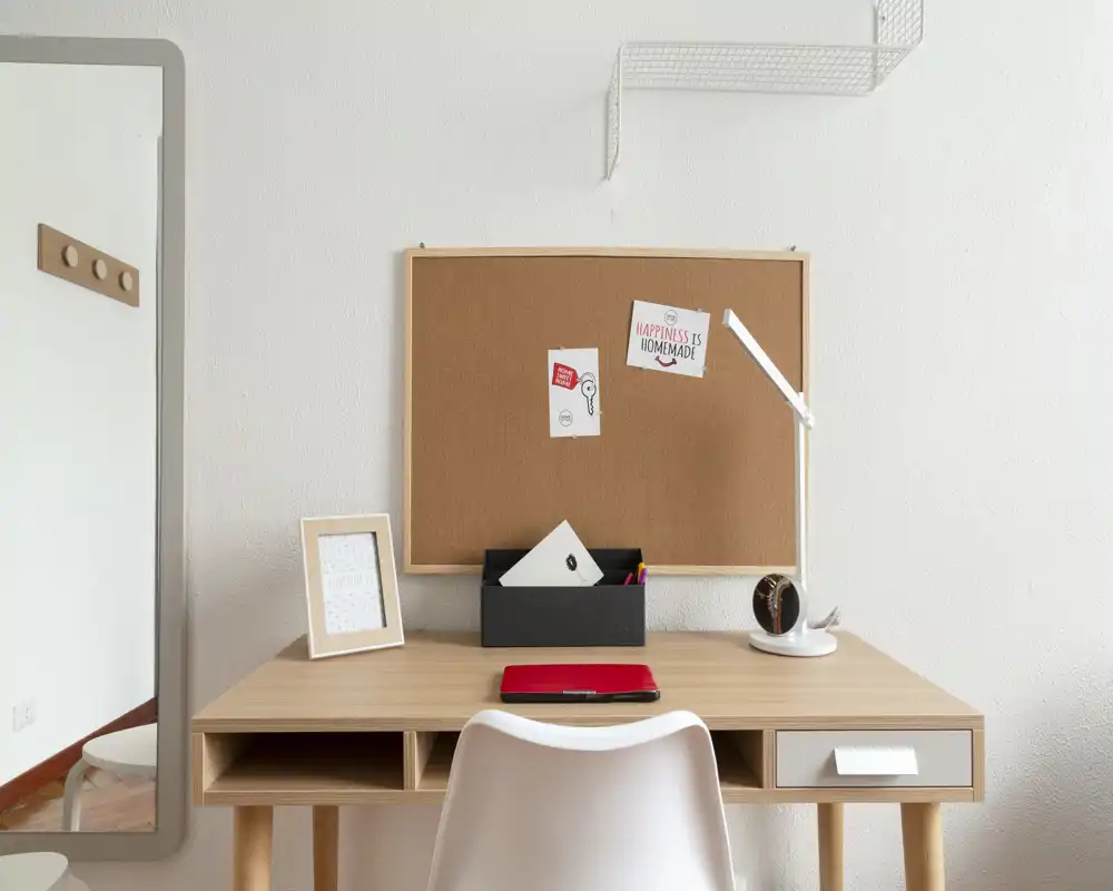 Spazio di lavoro ordinato con scrivania in legno, bacheca in sughero, lampada moderna e uno specchio laterale — ideale per smart working o studio.