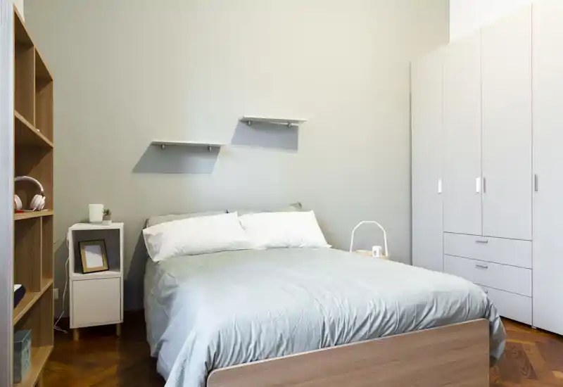 Camera da letto luminosa e ben arredata con letto centrale, comodini, mensole e un armadio a muro che offre ampio spazio di stoccaggio.