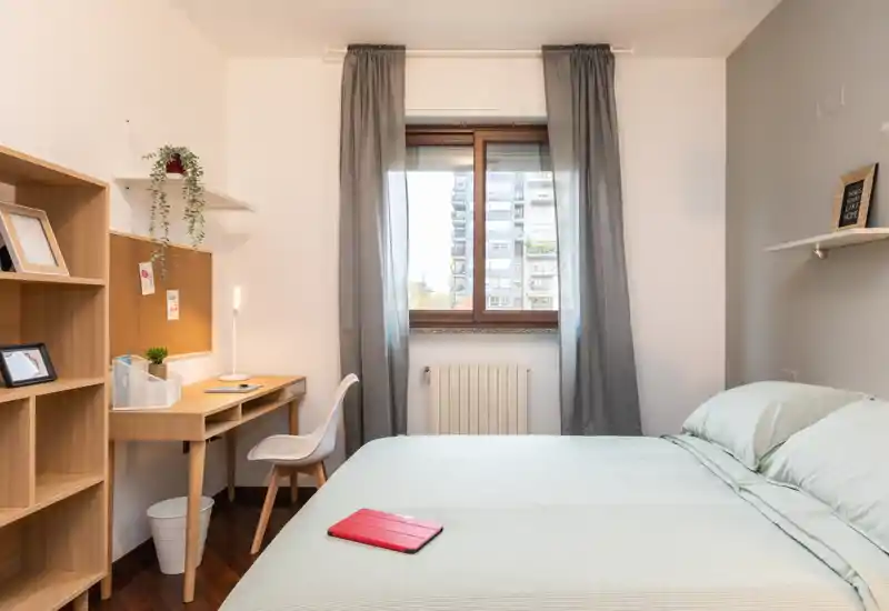 Camera da letto luminosa e ben arredata con un ampio letto, biancheria verde chiaro e una scrivania vicino alla finestra — ideale per riposo e lavoro da remoto.