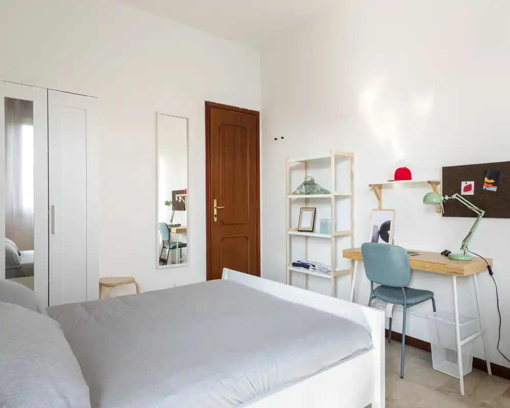 Dormitorio moderno y luminoso con cama doble bien hecha, armario y una pequeña zona de estudio — ideal para estudiantes o profesionales que buscan un espacio tranquilo y funcional.