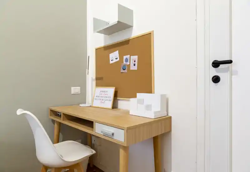 Bright, minimalist workspace with a wooden desk, white chair, cork noticeboard and small decorative objects — ideal for remote work or study.