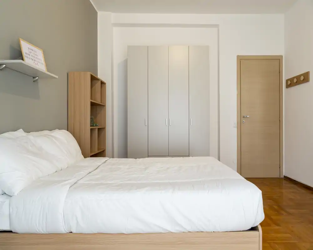 Dormitorio luminoso y minimalista con cama grande blanca, suelo de madera clara y armario empotrado — estilo moderno y tranquilo, ideal para alquileres vacacionales.
