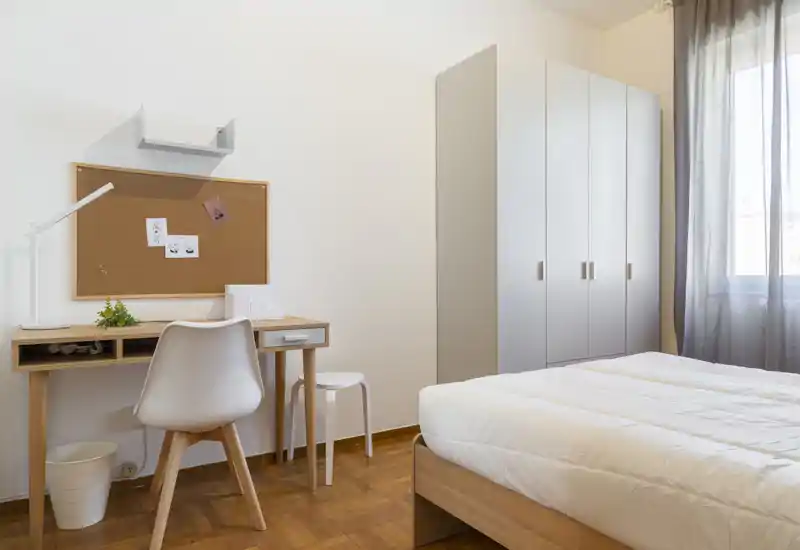 Dormitorio luminoso y minimalista con cama doble, armario y un pequeño escritorio — ideal para una persona o pareja que busca una habitación ordenada y bien iluminada.