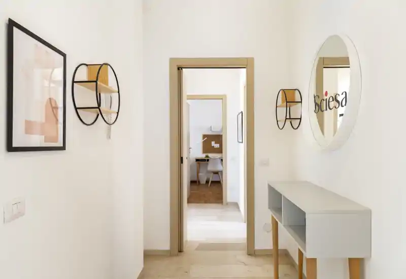 Bright, minimalist entrance hallway with a console table, round wall mirror and decorative shelves, leading to an interior room.