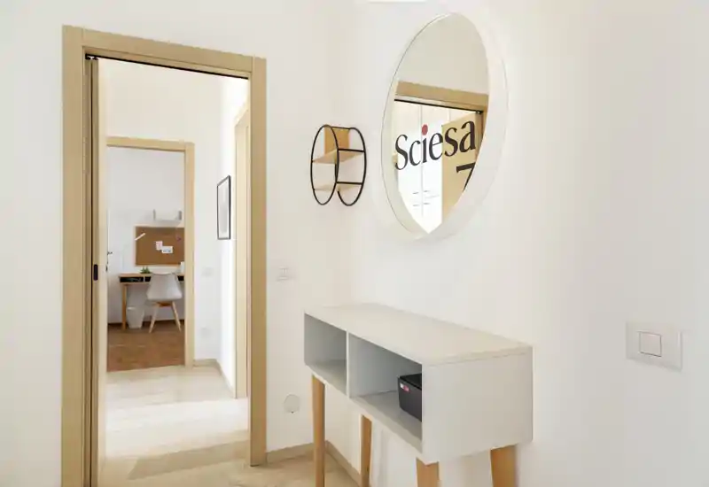 Bright, minimal entryway with a slim console table, round wall mirror and light wood trim — a welcoming, well-styled foyer area.