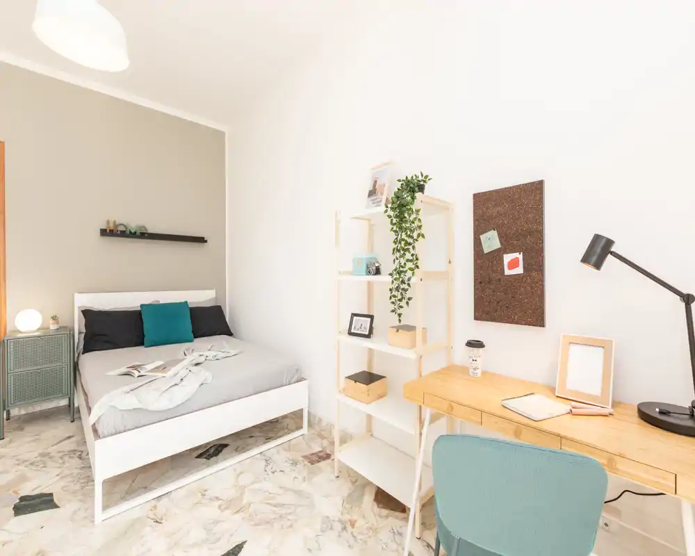 Dormitorio moderno y luminoso con cama doble, mesita, estantería y escritorio — tonos neutros y detalles acogedores que crean un ambiente tranquilo.