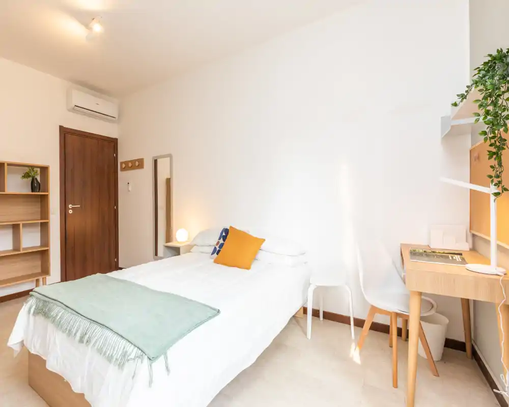 Camera singola luminosa e moderna con letto ben rifatto, scrivania e scaffalatura semplice — ideale per uno studente o un giovane professionista.