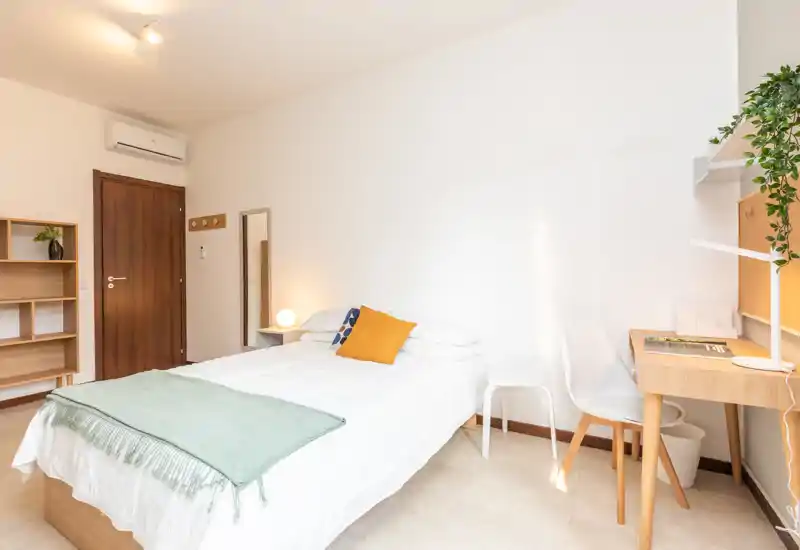 Dormitorio individual luminoso y moderno con cama bien hecha, escritorio y estantería simple — ideal para estudiante o joven profesional.
