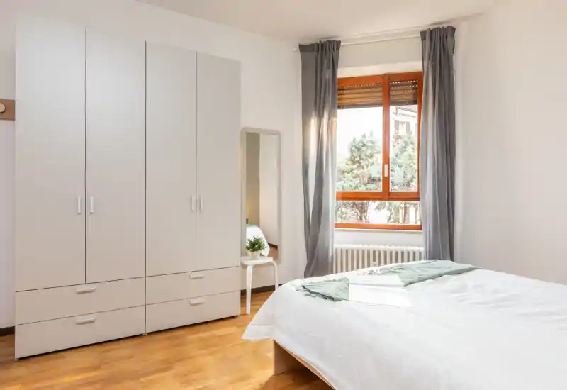 Camera da letto luminosa e minimal con letto matrimoniale, grande armadio e finestra che illumina naturalmente — ideale per annunci che vogliono valorizzare spazio e pulizia.