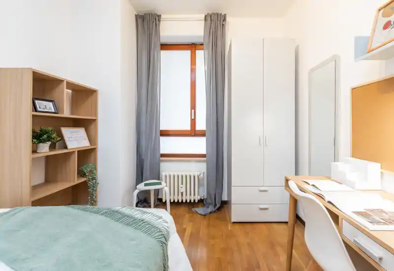 Camera da letto luminosa e ben arredata con letto singolo visibile, scrivania, armadio e mensole — ideale per uno studente o affitti brevi.
