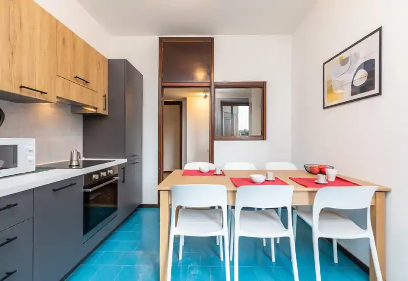 Modern fitted kitchen with dark lower cabinets, wood upper cabinets and a dining table set for four; bright, clean space ideal for small groups.