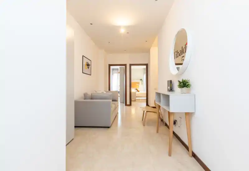 Bright, modern living area with a compact grey sofa, decorative mirror and console table; clean lines and neutral palette create a welcoming entry-lounge space.