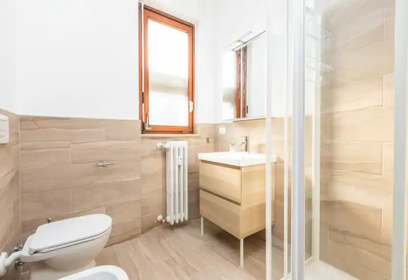 Bright, modern bathroom with wood-look tiles, a compact vanity with sink and mirror, toilet and shower cubicle—clean and well lit.