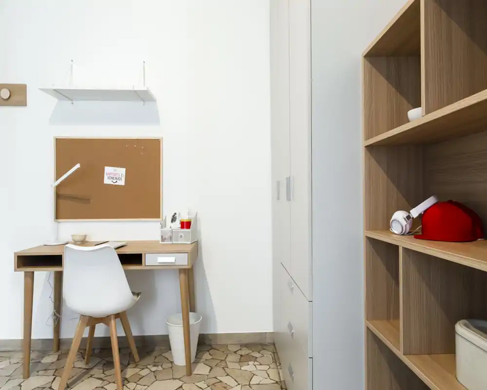 Angolo studio luminoso e minimal con scrivania in legno, sedia bianca, bacheca in sughero e scaffalatura — uno spazio ordinato ideale per lavorare o studiare da casa.