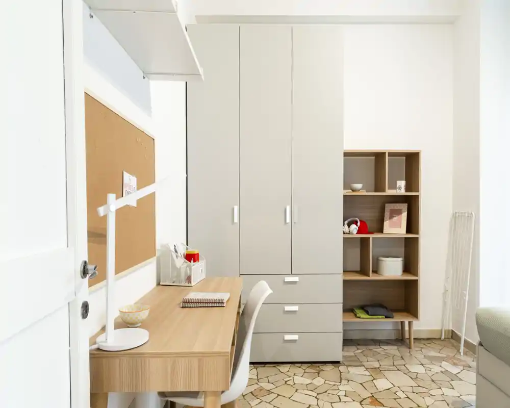 Angolo interno luminoso e minimale con scrivania in legno, sedia e grande armadio — un pratico spazio studio/parte della camera con scaffalatura e luce naturale calda.