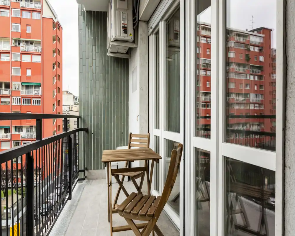 Balcone urbano con un tavolino e due sedie in legno, ideale per una colazione all'aperto con vista sulla città.