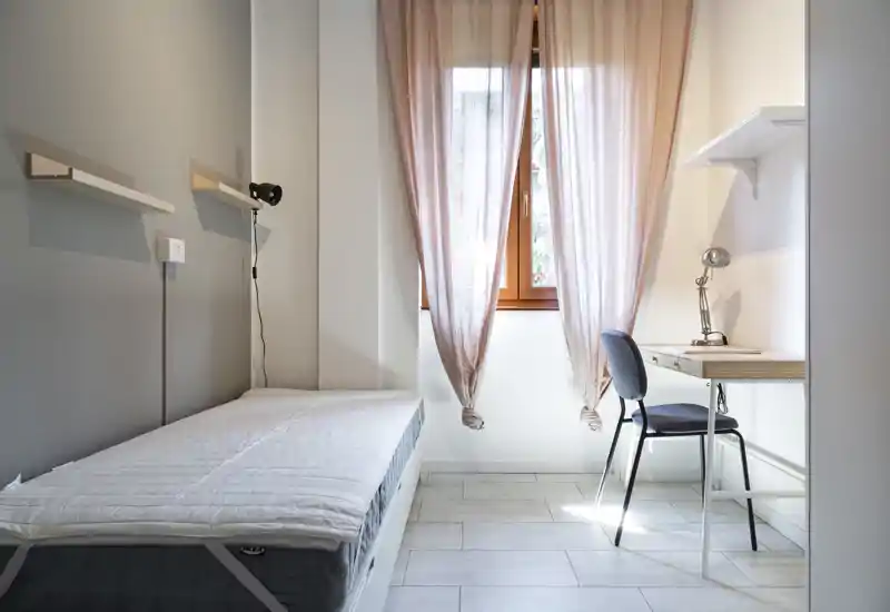 Sunny, minimalist single bedroom with a neatly made bed, desk and natural light from the window — ideal for a student or single occupant.