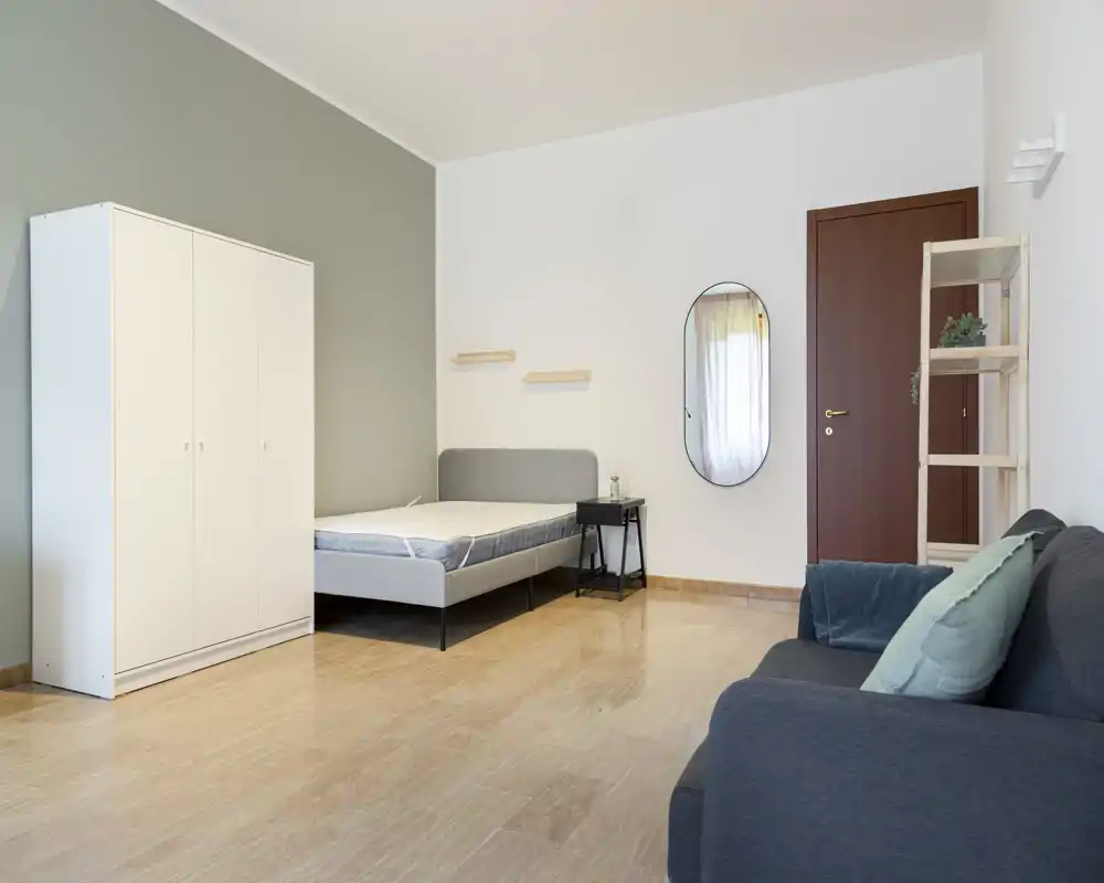 Bright, minimalist bedroom with a double bed, white wardrobe and a small bedside table; neutral tones and clean lines create a calm, airy atmosphere.
