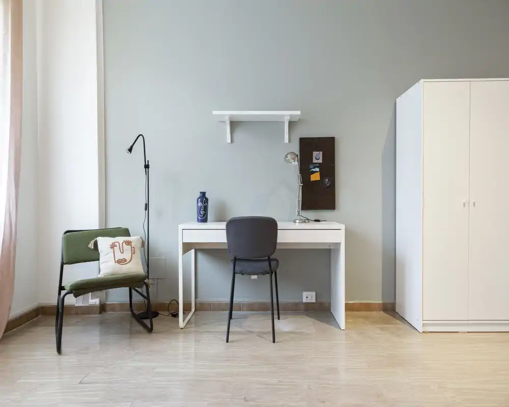 Minimal bedroom/studio corner with a desk, chair and wardrobe; clean, bright space suitable for single occupancy or a home office corner.