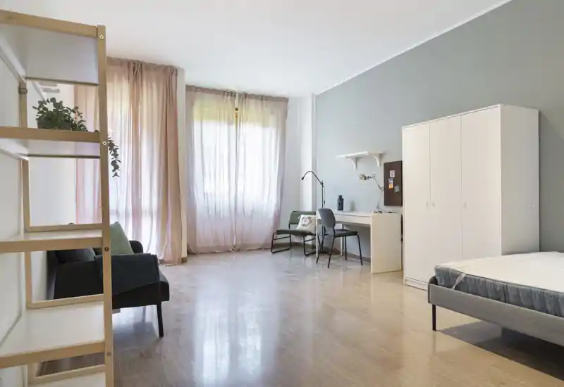 Amplio dormitorio con luz suave, cama visible, escritorio y armario; tonos neutros y cortinas translúcidas crean un ambiente moderno y ligero.