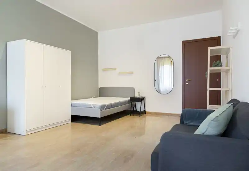 Dormitorio luminoso y minimalista con cama doble, armario blanco y una mesita; tonos neutros y líneas limpias crean una atmósfera tranquila y aireada.