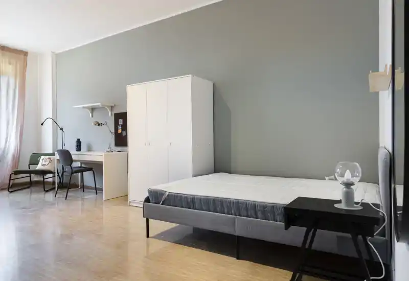 Dormitorio amplio y de estilo sencillo con cama doble, armario y zona de trabajo junto a la ventana; luz natural y tonos neutros que crean una atmósfera tranquila, ideal para anuncios.