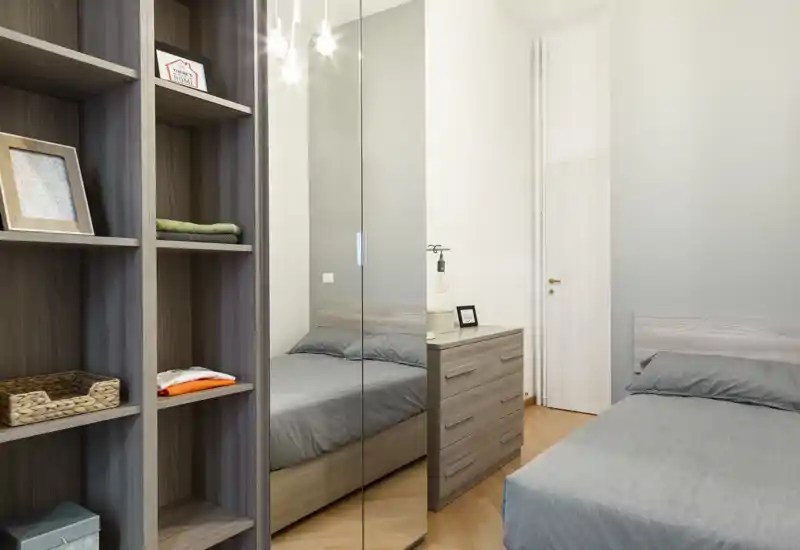 Camera da letto moderna e luminosa con letto matrimoniale, testiera in legno e comò coordinato; l'armadio a specchio amplia lo spazio visivo.