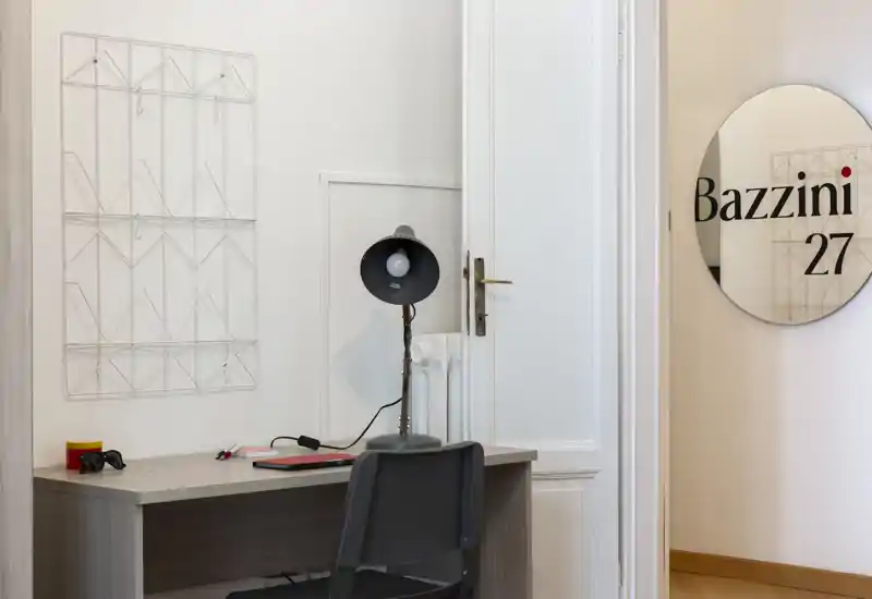 Angolo lavoro compatto con una scrivania semplice, sedia e lampada da tavolo su parete bianca — adatto per mostrare un piccolo ufficio domestico o angolo studio.