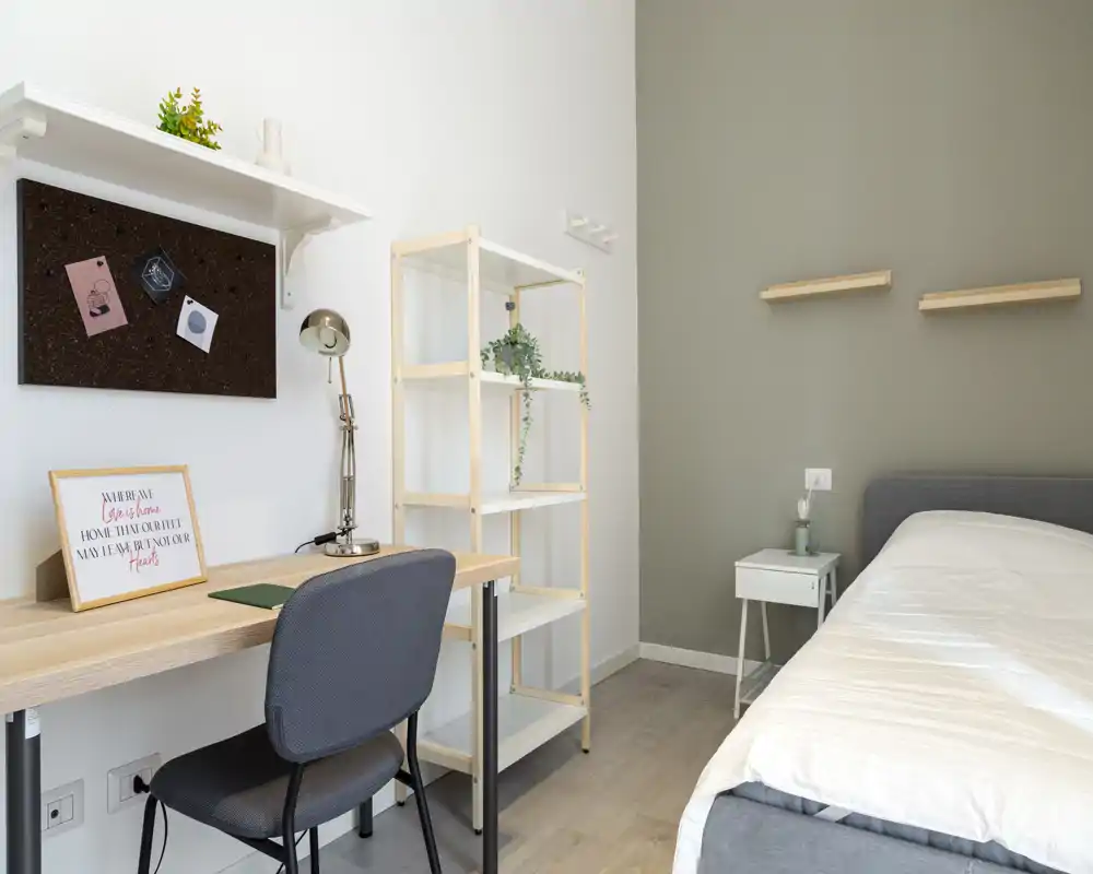 Camera da letto luminosa e moderna con un letto singolo, comodino e una scrivania funzionale — colori neutri, mensola e piante per un tocco accogliente.
