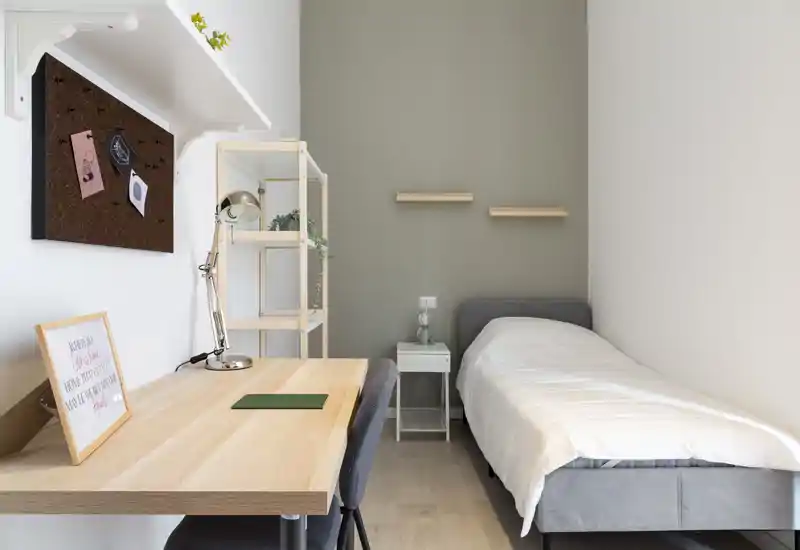 Bright, minimal single bedroom with a comfortable single bed, bedside table and a practical wooden desk — ideal for a student or solo traveler looking for a tidy, well-lit space.