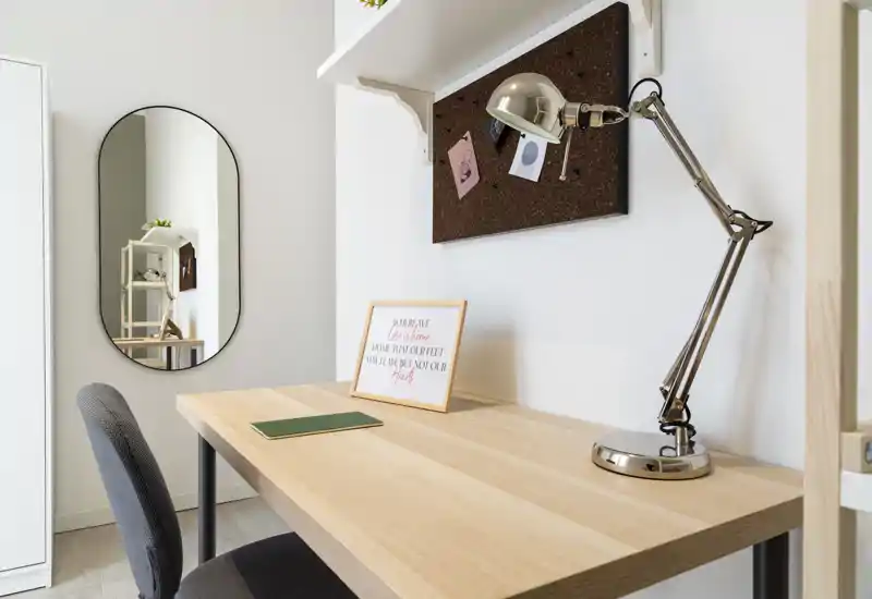 Bright, modern workspace corner with a wooden desk, adjustable desk lamp, cork noticeboard and a comfortable upholstered chair — ideal for remote work or study.