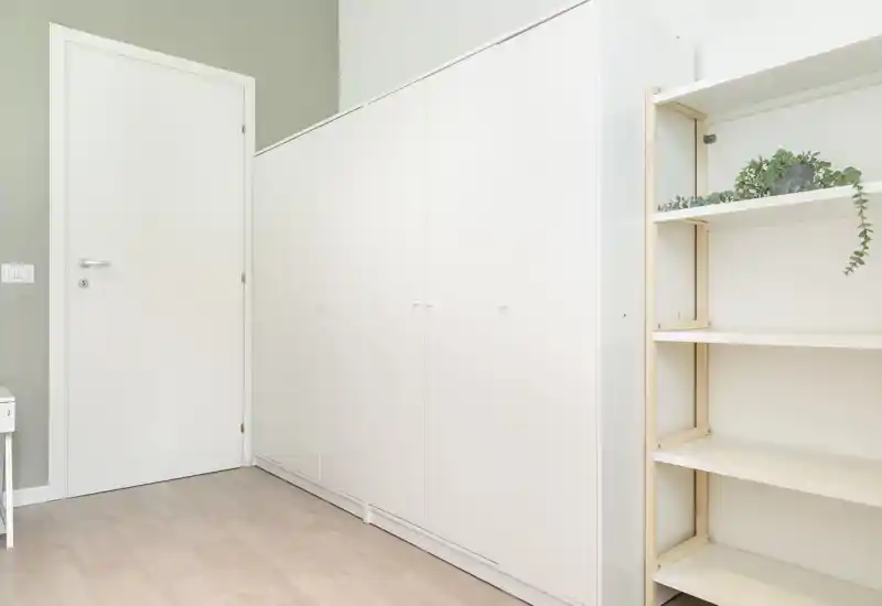 Entrée/couloir minimaliste avec placards encastrés blancs et étagères ouvertes. Sol clair et porte blanche fermée pour un espace d'accueil soigné.